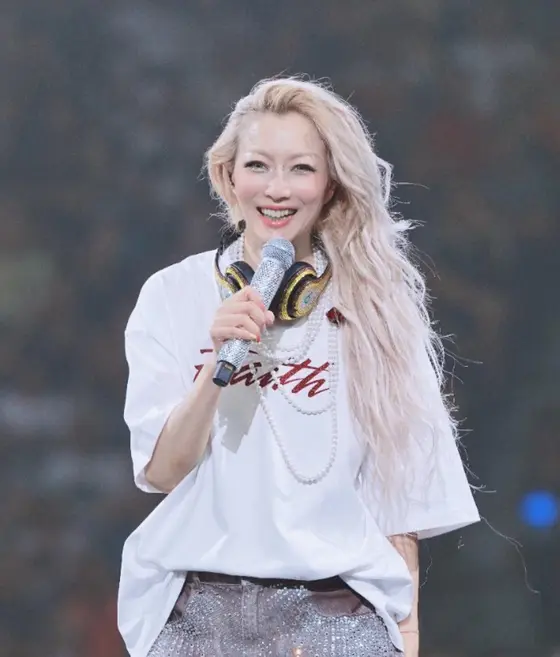 Sammi Cheng smiling mid-song, headphones round her neck