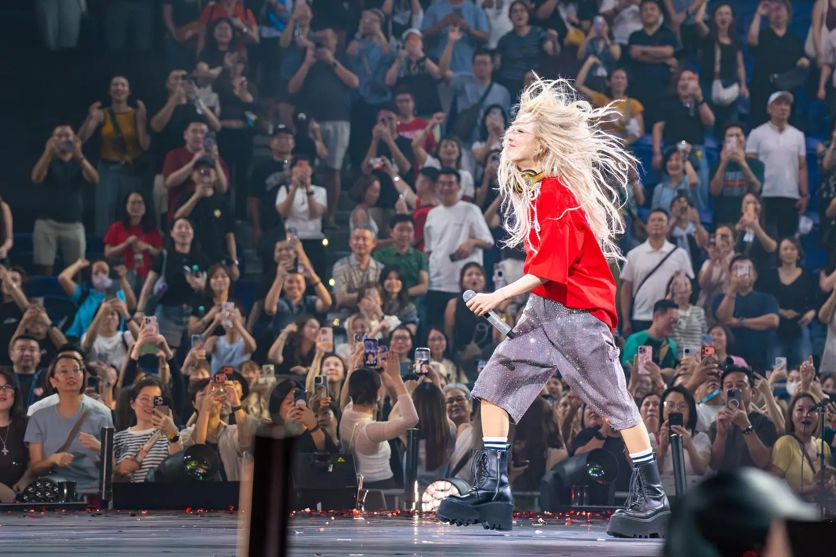 An artist on stage before a crowd holding up their phones
